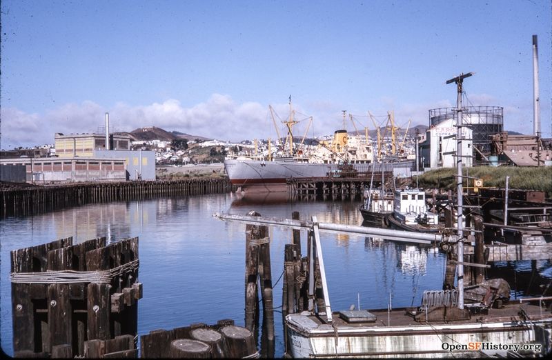 File:July 1963 Islais Creek View west from 3rd Street Bridge. Ship docked at Cargill Copra Plant, Bernal Heights in background left, Twin Peaks in background right wnp25.1676.jpg