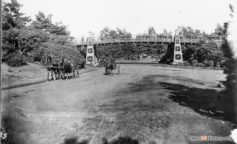 File:Ggp c 1890 View east on Middle Drive (now Nancy Pelosi) toward steel suspension bridge for pedestrians traveling between the old Bandshell (now Tennis Courts) and Flower Conservatory. Horses and wagons on roadway wnp26.1166.jpg