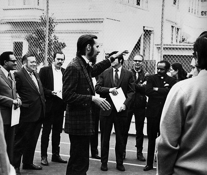 Plaid-jacketed-guy-w-goatee-addressing-MCO-and-dignitaries-in-schoolyard.jpg
