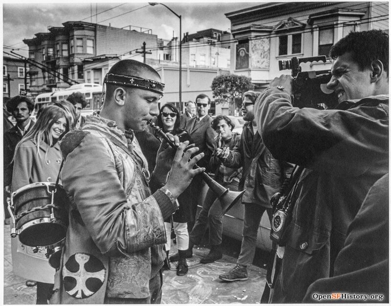 Hippie musician playing horn with video cameraman filming him and crowd watching wnp27.5954.jpg